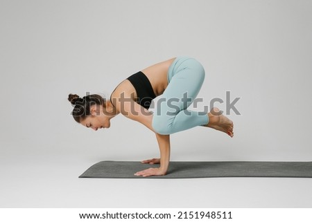 Young concentrated woman doing yoga exercises balancing on her arms. Mock-up.