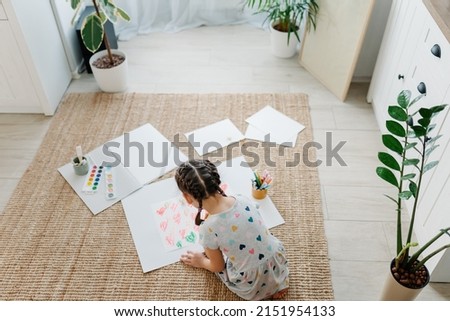 A girl draws hearts for his mother sitting on carpet floor in living room