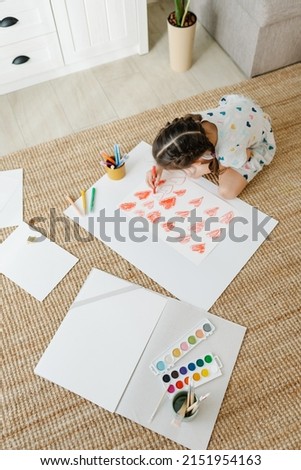 A girl draws hearts for his mother sitting on carpet floor in living room