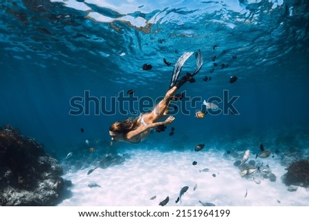 Beauty freediver lady with fins glides underwater with fishes in transparent blue ocean Royalty-Free Stock Photo #2151964199