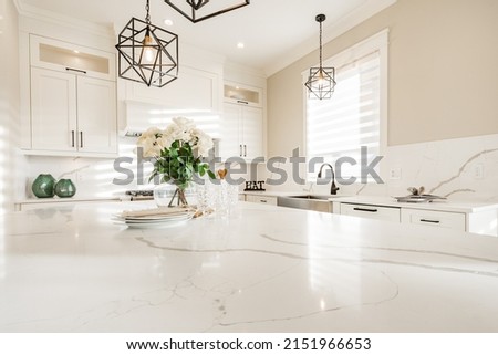 Warm white kitchen with expansive countertops island high end appliances spice kitchen black leather chair dining table wine fridge and office work station Royalty-Free Stock Photo #2151966653