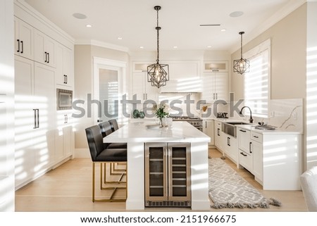 Warm white kitchen with expansive countertops island high end appliances spice kitchen black leather chair dining table wine fridge and office work station Royalty-Free Stock Photo #2151966675