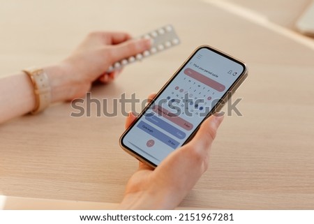 Close up of young woman calculating menstrual cycle using mobile app and holding birth control pills Royalty-Free Stock Photo #2151967281