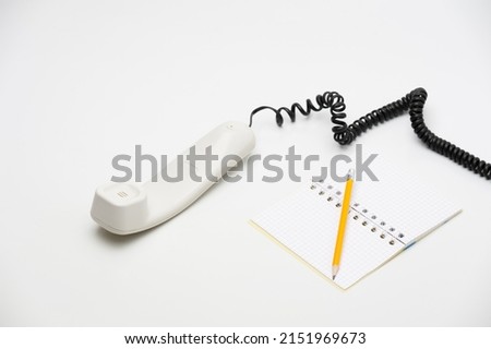 white handset with pencil and notebook lying on the white background