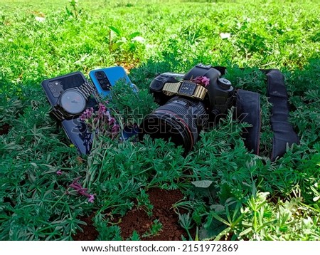 Professional camera and personal mobiles with a wristwatches among the grass. Photography. Professional photography.