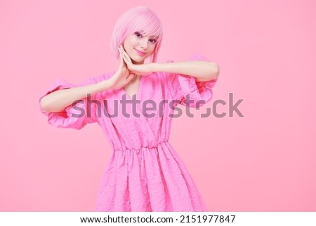 Beauty, fashion. Portrait of a cute teen girl with bright pink makeup and pink hair smiling and posing in fashionable pink dress. Pink background with copy space. 
