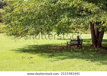 woman tourist in hat is resting on  bench in the shade of  tree in the park. Royalty-Free Stock Photo #2151981441