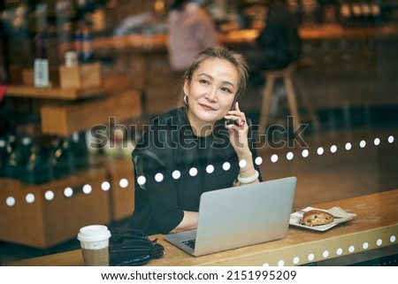mature asian business woman working in coffee shop using cellphone and laptop computer Royalty-Free Stock Photo #2151995209