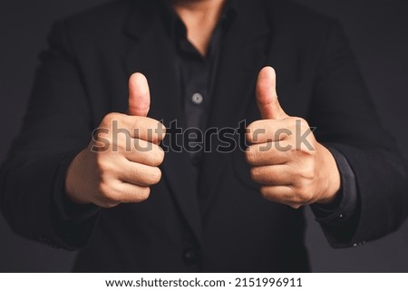 A businessman in a suit shows thumbs up with both hands while standing on gray background in the office. Customer service and satisfaction surveys concept. Close-up photo
