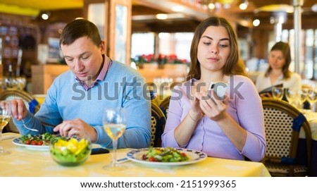Man and woman look at the screen of his smartphones during lunch in a restaurant
