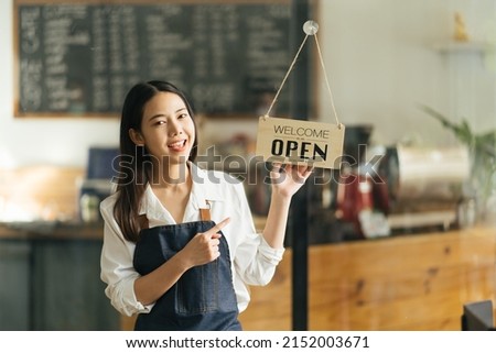 Asian Happy business woman is a waitress in an apron, the owner of the cafe stands at the door with a sign Open waiting for customers. Small business concept, cafes, and restaurants