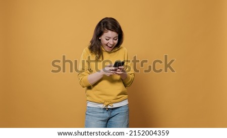 Portrait of casual woman holding smartphone texting having funny online conversation on social media messaging app in studio. Laughing person in her late 20s using digital touchscreen device.