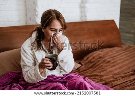 latin ill adult mature woman sneezing and using napkin for flu on bed at home in Mexico Latin America Royalty-Free Stock Photo #2152007581