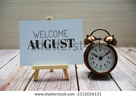 Welcome August text message with alarm clock on wooden background