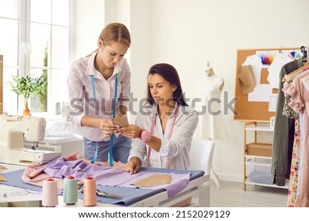 Female seamstresses work together in personal fashion atelier on client garment. Women tailors or designers sew design clothes in workshop together. Style and dressmaking concept. Small business. Royalty-Free Stock Photo #2152029129