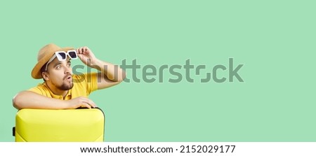 Wow, that's awesome. Portrait of surprised traveler with his holiday luggage on copy space banner. Young man on light green copyspace background looking at something with amazed happy face expression