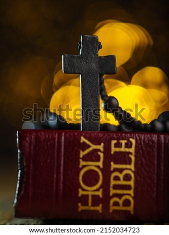 Catholic cross on a rosary on a book - the Holy Bible. Fantasy yellow background with twinkling lights. Prayer, faith, spirituality, meditation, catholicism. There are no people in the photo.