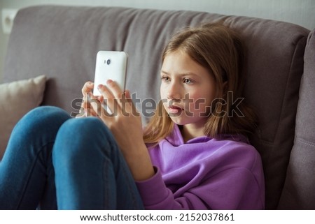 Upset depressed caucasian little kid girl holds mobile phone expresses sorrow and regret blames Royalty-Free Stock Photo #2152037861