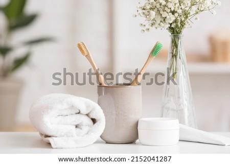 Holder with toothbrushes, jar of cream and rolled towel on table Royalty-Free Stock Photo #2152041287