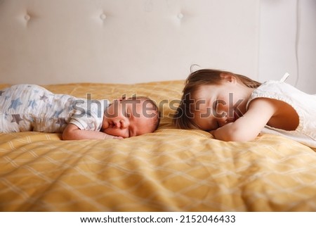 Cute bald chubby baby 2 months old and sister on bed in bedroom, baby siblings at home, toddler girl and baby in a cozy bedroom