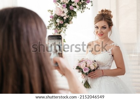 The girl takes a picture of the bride on the phone near the arch. High quality photo