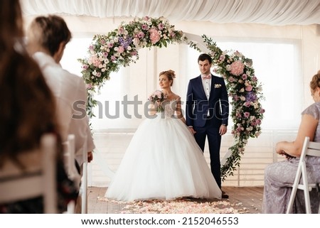 The bride and groom stand near the arch of roses at the wedding ceremony. Happy wedding couple. High quality photo Royalty-Free Stock Photo #2152046553
