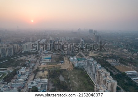 aerial drone shot passing over a building with homes, offices, shopping centers moving towards skyscapers in front of sunset showing the empty outskirts of the city of gurgaon India Asia Royalty-Free Stock Photo #2152048377