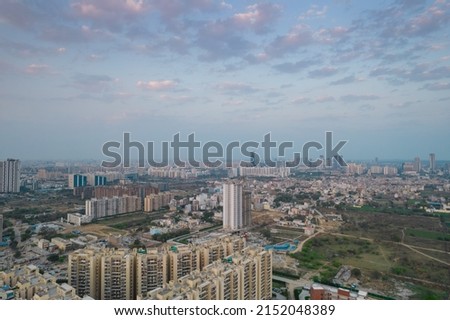aerial drone shot passing over a building with homes, offices, shopping centers moving towards skyscapers in front of sunset showing the empty outskirts of the city of gurgaon India Asia Royalty-Free Stock Photo #2152048389