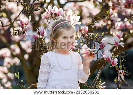 Cute spring fashion preschool girl under blossom magnolia tree. Little happy child and spring.