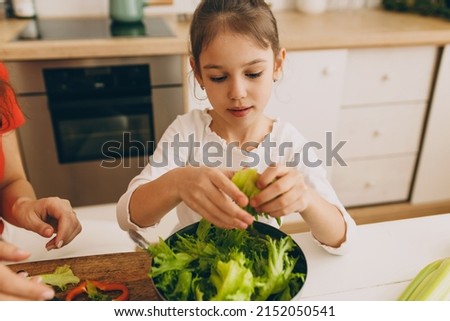 Close-up picture of cute concentrated child holding green organic romaine lettuce in hand, ready to put it in bowl to prepare healthy and delicious salad for dinner together with mom