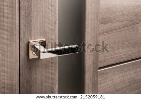 Close up of stylish silver chrome door handle on modern interior door. Stylish light brown door with frosted glass inserts. Concept of catalog of door handles for furniture store. Royalty-Free Stock Photo #2152059181