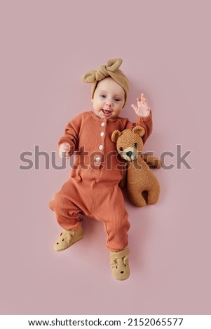 Adorable stylish baby smiling and hugging  toy bear against pink background. Cute infant in pajama with knitted toy