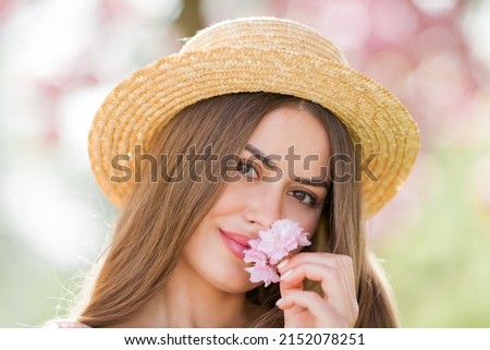 Spring portrait of a young beautiful woman in pink blossoms. Young beautiful model with long hair, in a wicker hat and a light dress near the cherry blossoms. Spring.