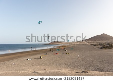 seascape, views of the yellow sand beach, bushes, people practicing kite surfing and Montaña Roja in the background. Paya Grande, El Medano, Tenerife, Canary Islands. Spain