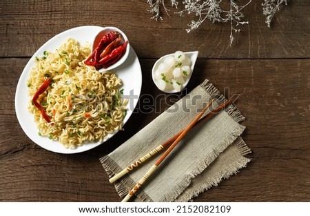 Instant noodles in a white plate with pickled vegetables on a wooden background.
