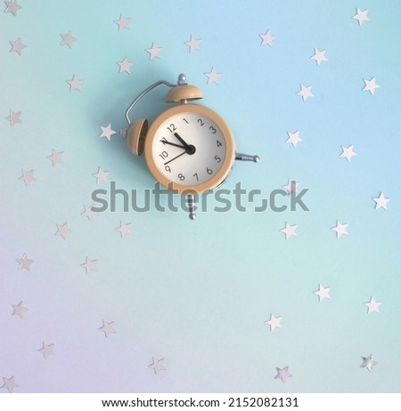 Party Time Layout with Little Beige Clock and Silver Confetti of Star Shape on a Vlue-Violet Gradient Background. No Text. Top-Down View. Flat Lay Composition ideal for Banner, Invitation, Card.