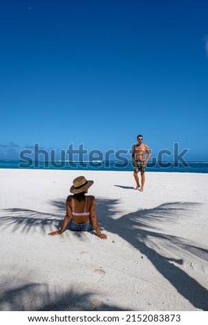 Tropical beach palm trees and white sand blue ocean and beach beds umbrellas, sun chairs, and parasols under a palm tree at a tropical beach. couple men and woman on tropical beach Le Morne Mauritius