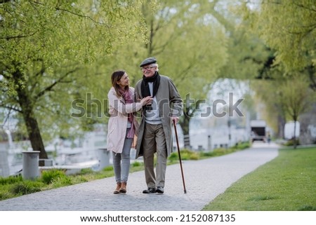 Happy senior man with walking stick and adult daughter outdoors on a walk in park. Royalty-Free Stock Photo #2152087135