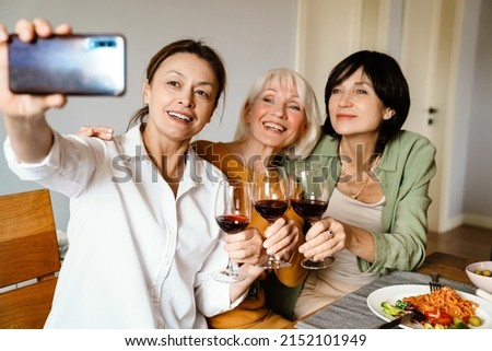 Mature three women taking selfie photo and drinking wine while having dinner at home