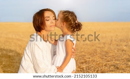 Daughter kisses her mom cheek standing wheat field. Little girl kiss mother Happy Mother's Day. Happy family relationship outdoor. Dressed white. Caucasian female woman 35 years and girl 5 years old