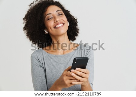 Young black woman in earphones smiling and using mobile phone isolated over white background Royalty-Free Stock Photo #2152110789
