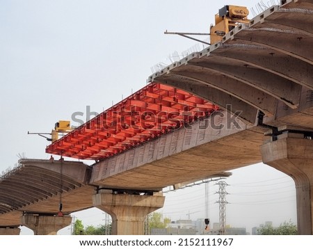under construction bridge with red supports placed for metro train tracks, expressway to help solve traffic problem of delhi India gurgaon etc Royalty-Free Stock Photo #2152111967