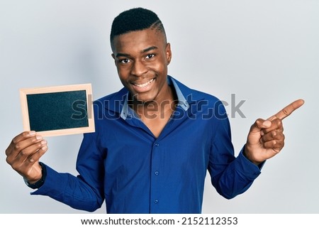 Young african american man holding empty frame smiling happy pointing with hand and finger to the side 
