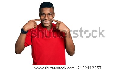 Young african american man wearing casual red t shirt smiling cheerful showing and pointing with fingers teeth and mouth. dental health concept. 