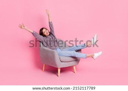 Portrait of attractive cute cheerful girl sitting in armchair rising hands up isolated over pink pastel color background Royalty-Free Stock Photo #2152117789