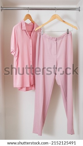 Pastel pink monochrome fashion look hanging on wooden rack in white wardrobe. Shopping , monochrome look concept. Royalty-Free Stock Photo #2152125491