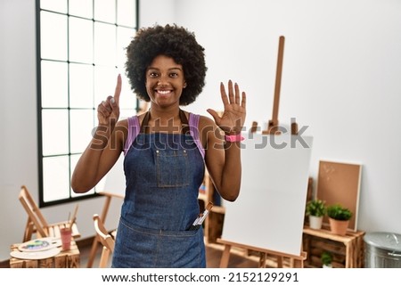 Young african american woman with afro hair at art studio showing and pointing up with fingers number six while smiling confident and happy. 