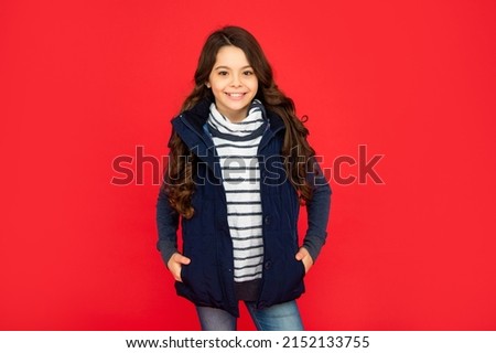 winter fashion. happy kid with curly hair in puffer waistcoat. teen girl on red background. Royalty-Free Stock Photo #2152133755