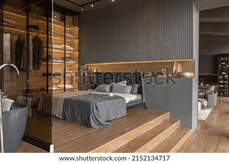 bedroom and freestanding bath behind a glass partition in a chic expensive interior of a luxury home with a dark modern design with wood trim and led light Royalty-Free Stock Photo #2152134717