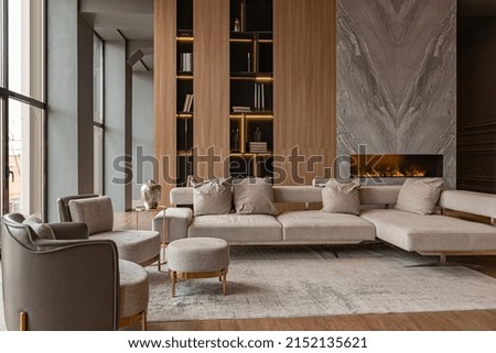 living room, marble wall fireplace and stylish bookcase to the ceiling in a chic expensive interior of a luxurious country house with a modern design with wood and led light, gray furniturу Royalty-Free Stock Photo #2152135621